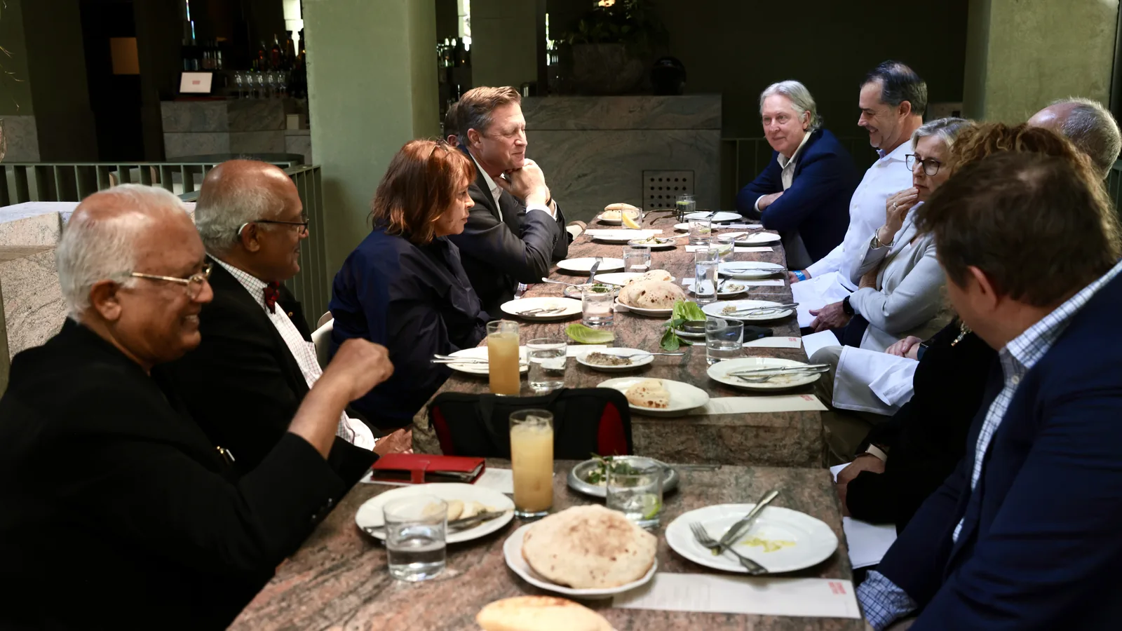 Twelve consultants seated along a long stone table at a Mindhive members' lunch, talking across the plates in two and threes.